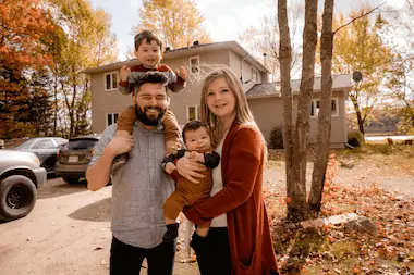 Familia feliz de dos padres y dos hijos, sonriendo a la cámara enfrente de su casa